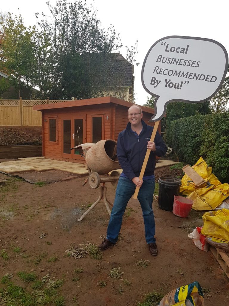 Builder_Standing in Sidmouth garden holding sign 'local businesses recommended by you'