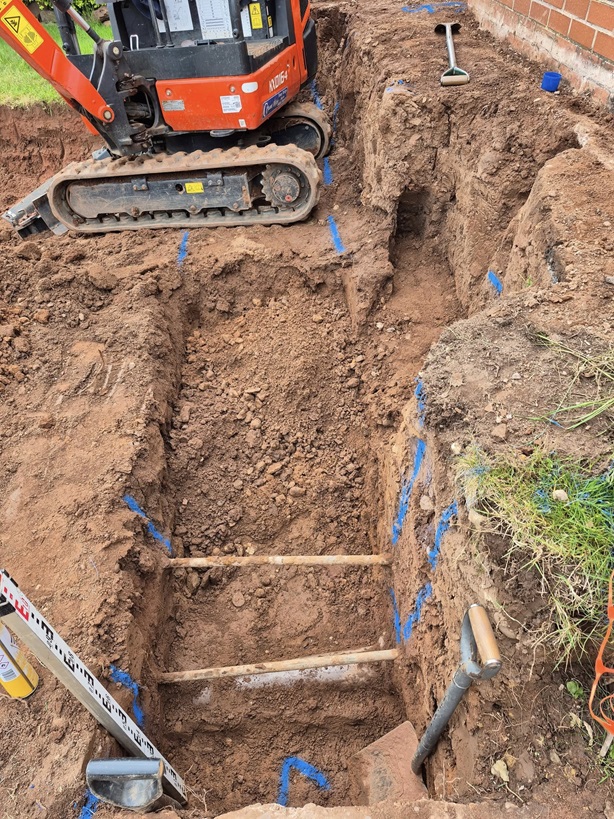 Mini digger above newly dug trench.