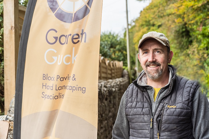 Smiling driveway installer in front of branded flag.